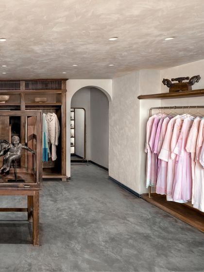 The main retail area at Eka features custom-designed wooden wardrobes and a unique glass display case for accessories. The arched doorway and lime-washed walls add to the feeling of being in a familiar, personal space rather than a conventional store.