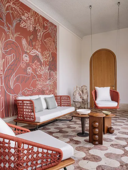 This vibrant terrace features a woven sofa and a hanging swing chair, both designed for outdoor living. The burnt orange of the furniture complements a stunning, large-scale wall mural, creating an inviting and artistic outdoor lounge space.