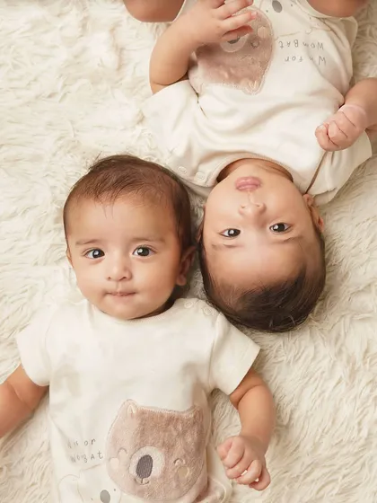 A playful shot of twin babies lying on a fluffy rug in matching bear-themed outfits. Their curious expressions are just adorable.