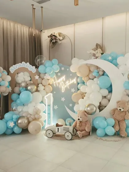 A dreamy and elegant "Twinkle Twinkle Little Star" birthday theme. This setup uses a soft blue and neutral color palette, with a large crescent moon prop, teddy bears floating on clouds, and a "Happy Birthday" neon sign to create a serene and magical photo backdrop.
