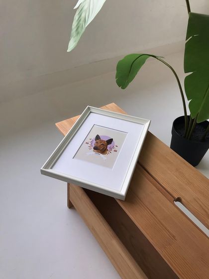 The framed Chiku portrait resting on a wooden bench in my studio, surrounded by plants. It shows how the art can bring a personal touch to any space.