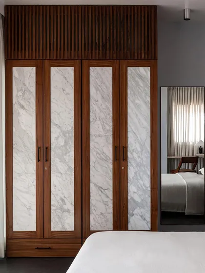 Another look at the custom wardrobe with marble-infilled shutters. The reflection in the mirror shows how the wardrobe becomes an integral part of the bedroom's serene and sophisticated design.