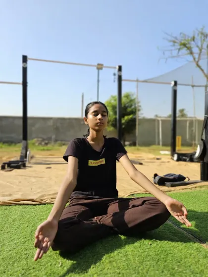 A young athlete practices the lotus pose (Padmasana) outdoors, finding stillness and focus amidst the training environment.