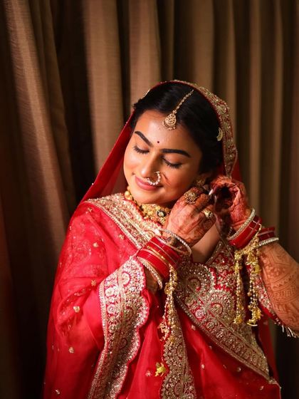 A classic bridal portrait in a timeless red outfit, showing the final touches being put on the earrings.