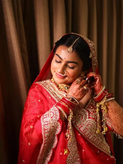 A classic bridal portrait in a timeless red outfit, showing the final touches being put on the earrings.