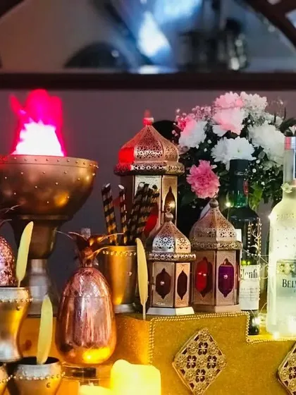 A close-up of the rich textures and warm lighting of the Sufi theme. Brass goblets, glowing lanterns, and a dramatic flame effect create a captivating and opulent bar front.