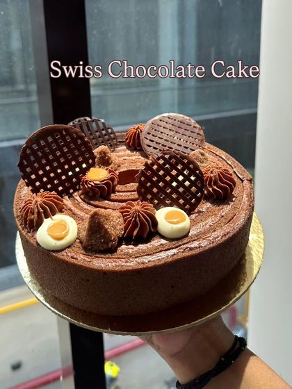 A close-up of my classic Swiss Chocolate Cake. It's decorated with delicate chocolate work, piped rosettes, and a rich, smooth finish.