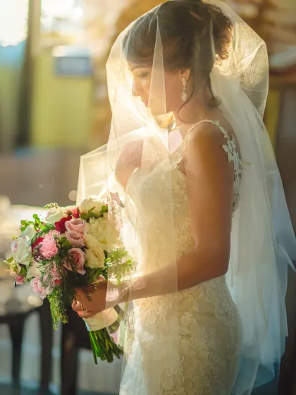 A bride is bathed in beautiful, soft light, holding her bouquet. This portrait captures a quiet, contemplative moment, highlighting her elegance and the delicate details of her veil.