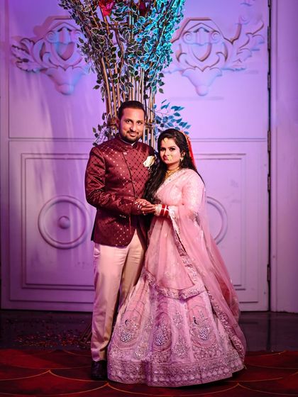 A classic posed portrait of the couple on their wedding day. Dressed in beautiful pink and maroon outfits, this shot captures their elegance and happiness against the backdrop of their wedding decor.