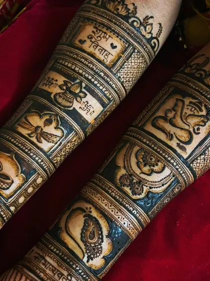 A close-up of the forearm portion of a bridal design. It showcases auspicious wedding symbols like 'Shubh Vivah', a 'kalash' (ceremonial pot), diyas, and Lord Ganesha.