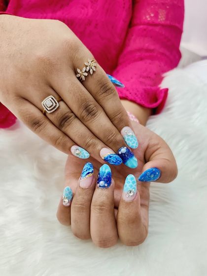 Catch the waves of style with these dreamy beach shell nails. This set features a stunning blue marble effect, glitter, and crystal accents for a look inspired by the ocean.