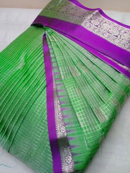 A bright green saree with a purple and silver border. The pleats are crisp and the saree is ready to be draped in minutes.