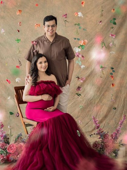 A beautiful portrait of an expecting couple, seated amidst a dreamy floral setup in the studio.