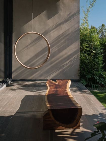 A sculptural wooden bench and a circular hanging art piece on the veranda. These elements create a beautiful, artistic vignette that plays with form and shadow.
