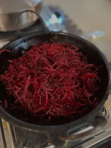 A vibrant beetroot stir-fry cooking in a traditional iron pan. Our recipes are simple, using minimal oil and spices to let the natural flavors of the vegetables shine.