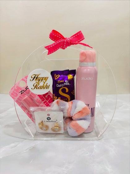 A lovely Rakhi hamper for a sister, filled with self-care goodies. It includes a body spray, earrings, a lip balm, a soft scrunchie, and Dairy Milk Silk, all packed in a cute acrylic bag.