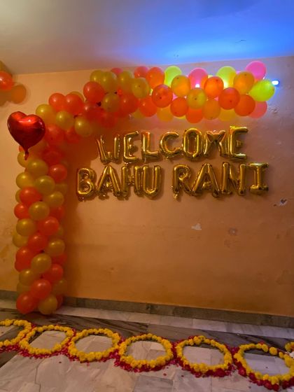A closer look at the 'Welcome Bahu Rani' balloon arrangement. The gold foil letters stand out against the orange and yellow balloon arch, creating a festive and celebratory photo opportunity.