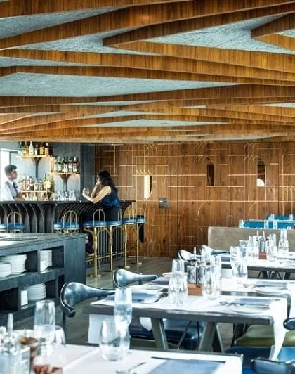 The main dining hall of the Queensline Sea Yah floating restaurant. To address the challenge of a low ceiling, we developed a repeating, tree-like structural element from Indian Teak wood, which gives the long space character and a sense of rhythm.