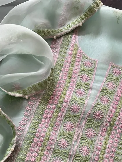 A vibrant pure organza suit in a soft sea green, adorned with intricate pink and green threadwork. The neckline features delicate work, and the dupatta is finished with a border of pearls.