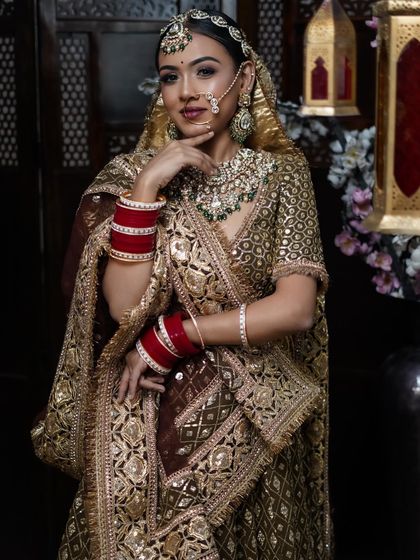 A classic bridal portrait in a gold and maroon lehenga, showcasing smoky eyes and traditional jewelry.