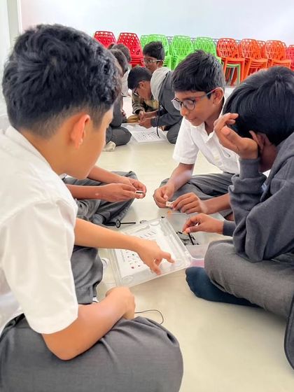 A group of students from Sadhu Vaswani International School works together, pointing out details in their instruction manual and on their model.