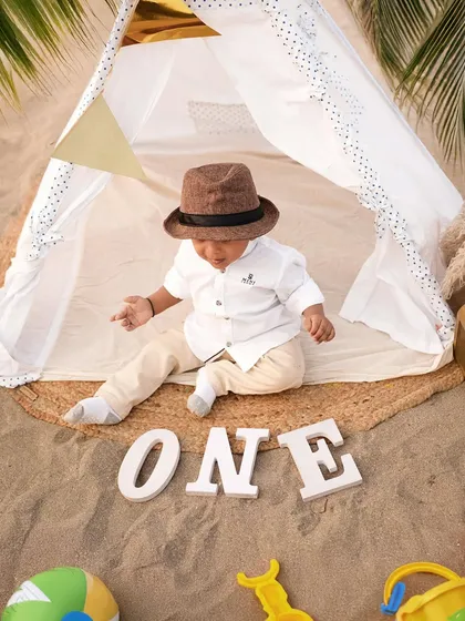 Marking a first birthday on the beach. This little one sits inside a teepee with "ONE" spelled out in the sand, a perfect setup for a memorable outdoor milestone session.