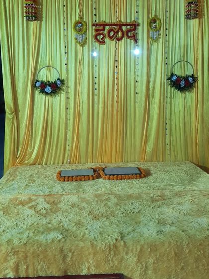 A simple and traditional Haldi stage with a low seating arrangement and a backdrop decorated with hanging ornaments.