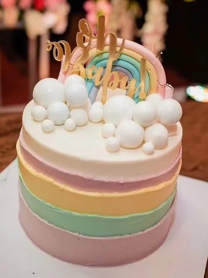 A pastel rainbow cake with fluffy cloud decorations and a "Oh Baby" topper, perfect for a baby shower.