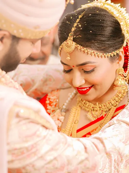 A close-up shot filled with emotion. The bride's joyful smile and bright red lipstick are the focus, capturing a moment of pure happiness during the wedding rituals.