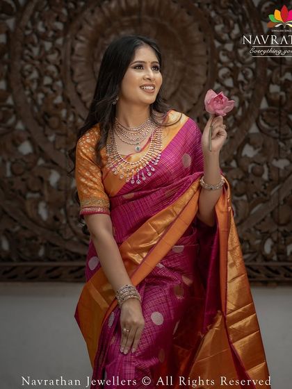 Our client Komal looks beautiful in this bright pink and orange Kanchipuram silk saree, holding a lotus flower in this artistic shoot.