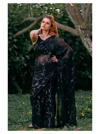 A full-length shot showing the entire saree against the lush greenery, highlighting its sparkle and flow.