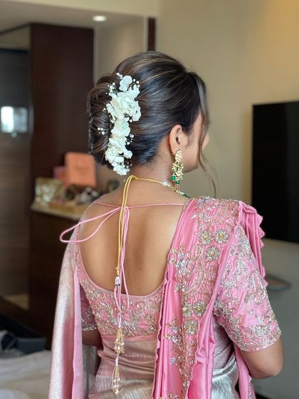 A soft, romantic low bun with interwoven sections and highlighted strands. I adorned this updo with a cascade of white flowers for a delicate and graceful look, ideal for a wedding guest or bridesmaid.