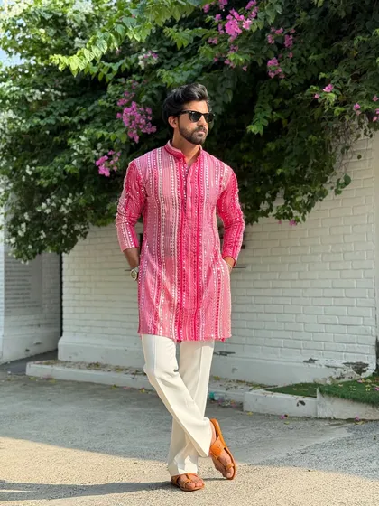 A relaxed, full-length view of the pink striped kurta paired with white trousers and traditional leather sandals. This look embodies effortless festive style, perfect for a sunny day event.