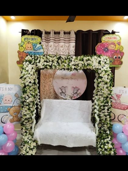 A beautiful baby shower decoration for a home, featuring a floral arch over a swing. The 'It's a Boy' and 'It's a Girl' props make it a versatile setup.