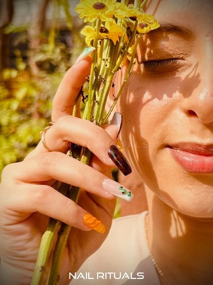 A summer escape at your fingertips. This image showcases a vibrant, multi-design manicure held against a backdrop of yellow flowers.
