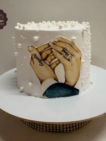 A very personal anniversary cake featuring an edible image of the couple's hands with their names tattooed. The cake is finished with simple whipped cream and delicate pearl details.