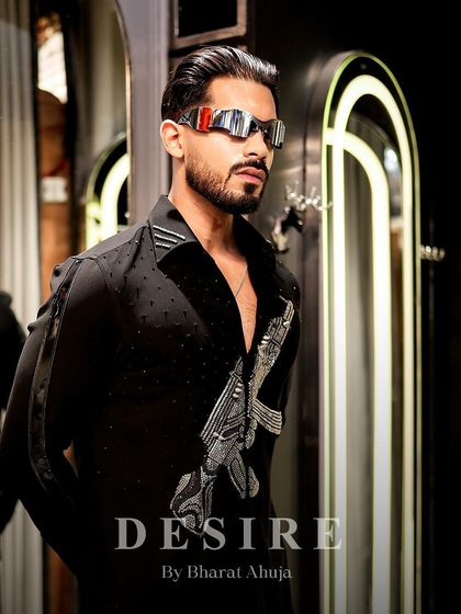 Locked, loaded, and luxe. This portrait showcases the futuristic sunglasses and the bold, embroidered gun motif on the black shirt.