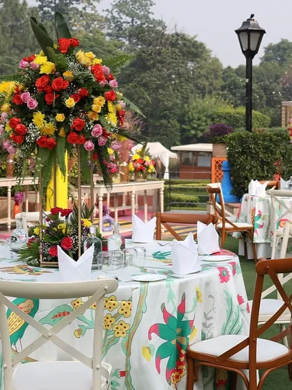 A colorful table setup with printed tablecloths and bright floral centerpieces for a carnival-themed event.