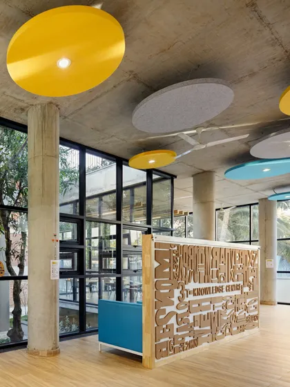 The reception desk at a school, featuring a custom-designed front panel with typographic art. The space is bright and open, with colorful ceiling panels and views of an internal courtyard.