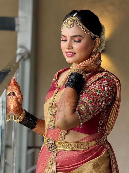 A serene portrait of the bride by the railing. The soft lighting highlights the beautiful texture of her saree and the flawless finish of her makeup.