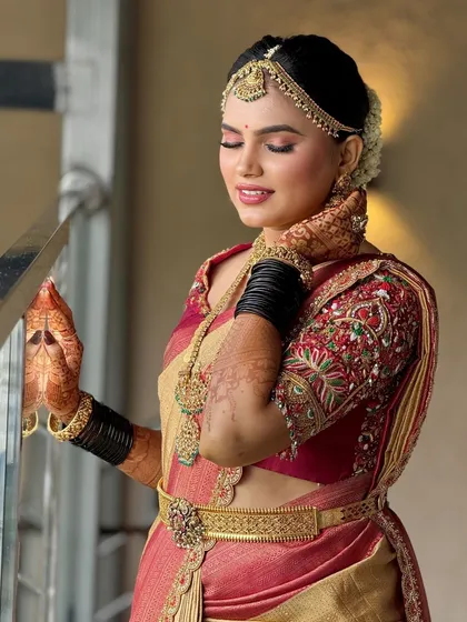 A serene portrait of the bride by the railing. The soft lighting highlights the beautiful texture of her saree and the flawless finish of her makeup.