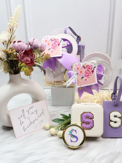 A beautiful bridesmaid proposal hamper in a pastel purple theme. This gift includes a personalized jewelry organizer, luggage tag, and pocket mirror, presented with a "Will you be my bridesmaid?" card.