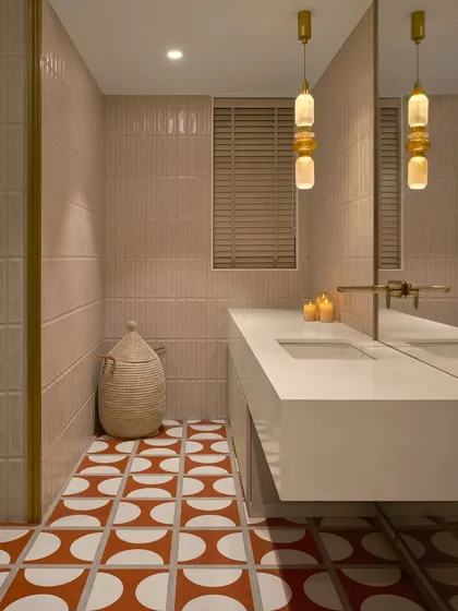 This bathroom combines soft pink vertical tiles on the walls with a bold orange and white patterned tile on the floor. A woven jute laundry basket adds a natural, textural element.