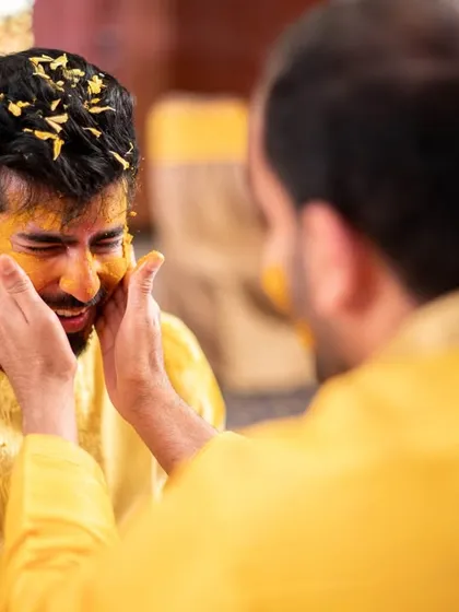 A friend enthusiastically applying haldi to the groom's face.