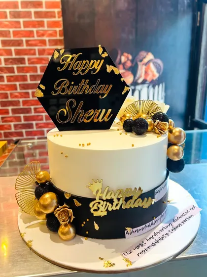 A sophisticated black and white cake with a hexagonal topper and gold and black decorative spheres.