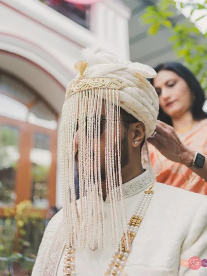 A mother's hands adjusting the groom's safa, a moment of love and tradition captured in detail.