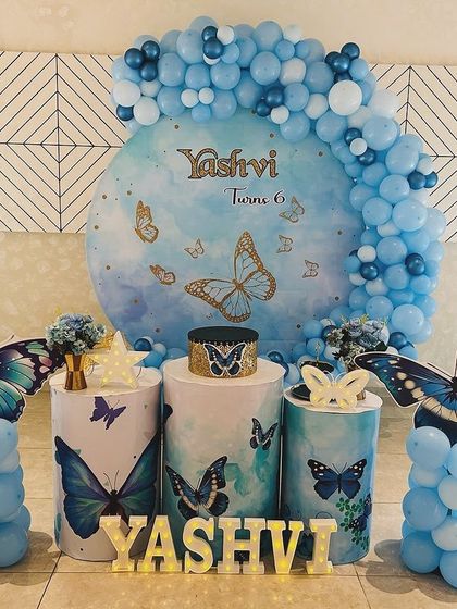 An elegant blue butterfly theme for a 6th birthday. This setup features a circular backdrop with blue butterflies, themed cake stands, and large 3D butterfly props.