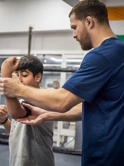Technique is everything. A coach provides hands-on correction to ensure this young student understands the mechanics of a defensive block. This attention to detail is crucial for effective and safe martial arts training.