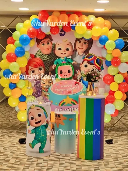 A full and festive Cocomelon themed birthday circle. The round backdrop features the whole Cocomelon family, surrounded by a rainbow balloon garland and themed cake stands.