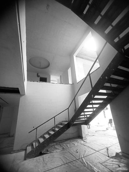 Looking up at the double-height space from the lower level during construction, showing the ceiling details and staircase structure taking shape.